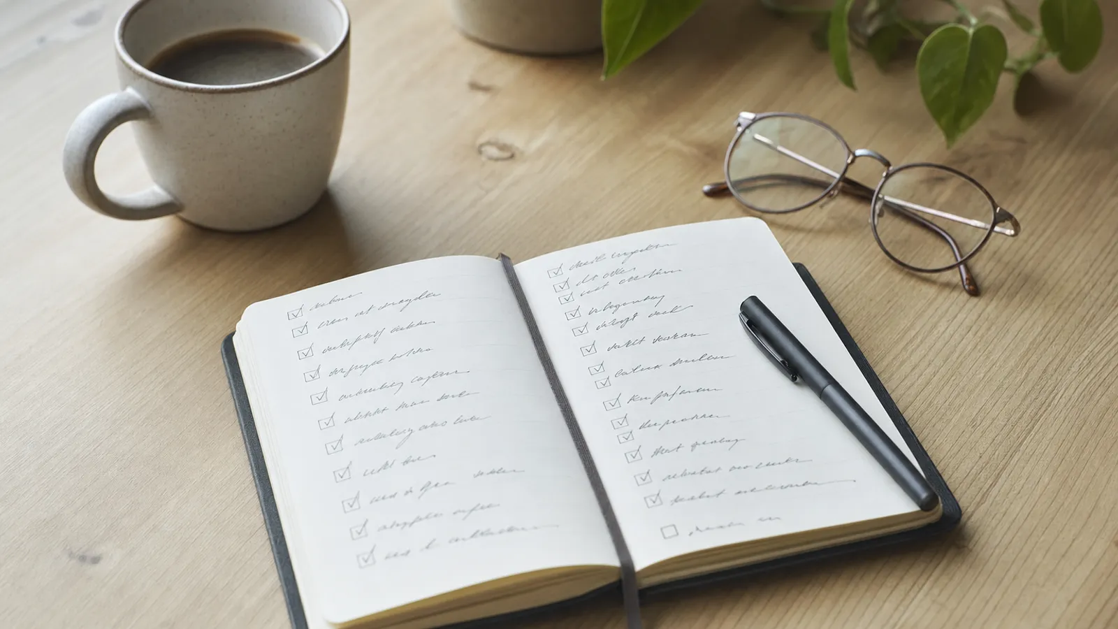 Notizbuch mit Checkliste und Kaffeetasse auf hellem Holztisch